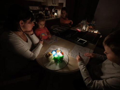 A mother and her three children are sitting around a kitchen table while the power is out with candles lit.