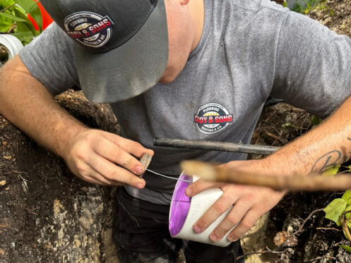 A plumber is applying solvent primer to a PVC pipe.